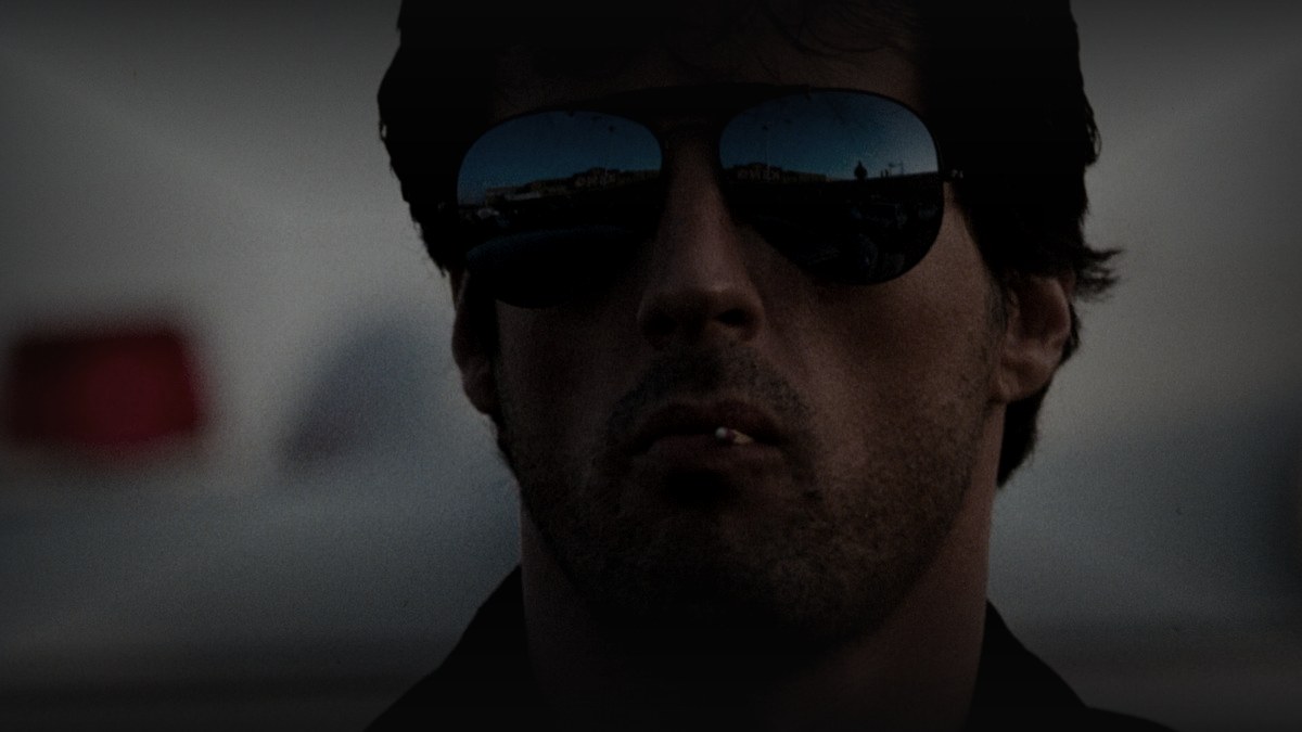 Still from Cobra (1986) — 16:9 still from Letterboxd (1200x675 crop variant), baked through scripts/bake_dark_photo.py at default factor 0.45