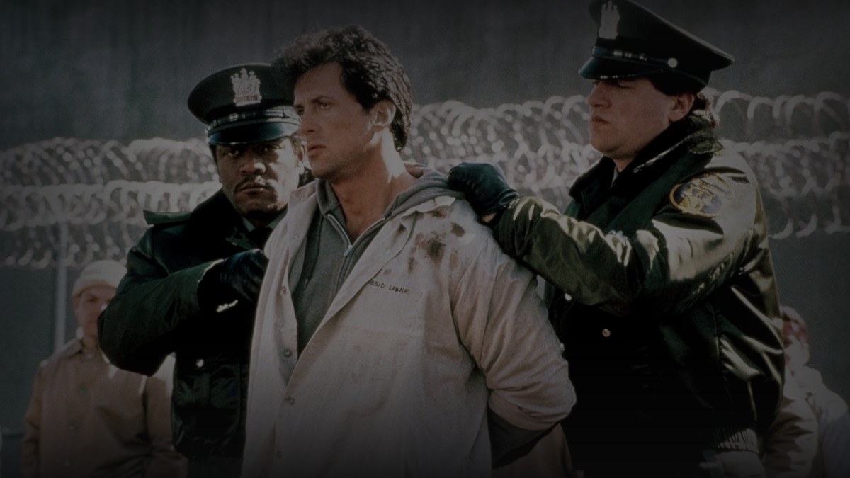 Still from Lock Up (1989) — 16:9 still from Letterboxd (1200x675 crop variant), baked through scripts/bake_dark_photo.py at default factor 0.45